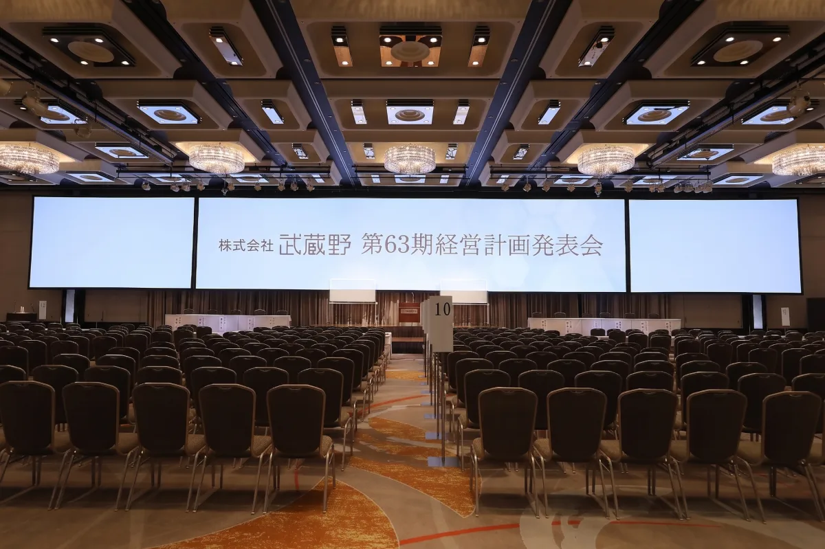 株式会社武蔵野 第63期経営計画発表会の会場。大きなスクリーンに会社名と発表会名が映され、整然と椅子が並んでいる